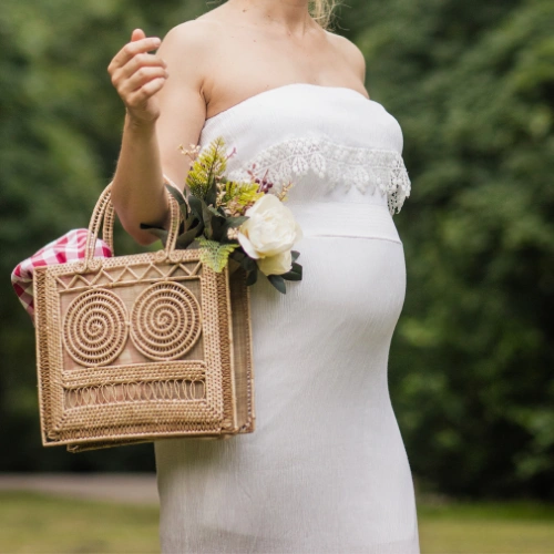 Pregnant woman outdoors holding flowers and a bag, representing motherhood